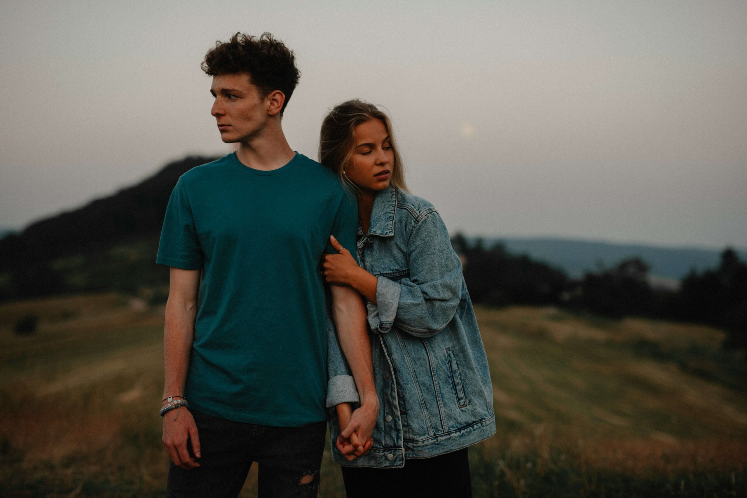 Two young adults, one grasping onto the other's arm, standing outside on a gray day.