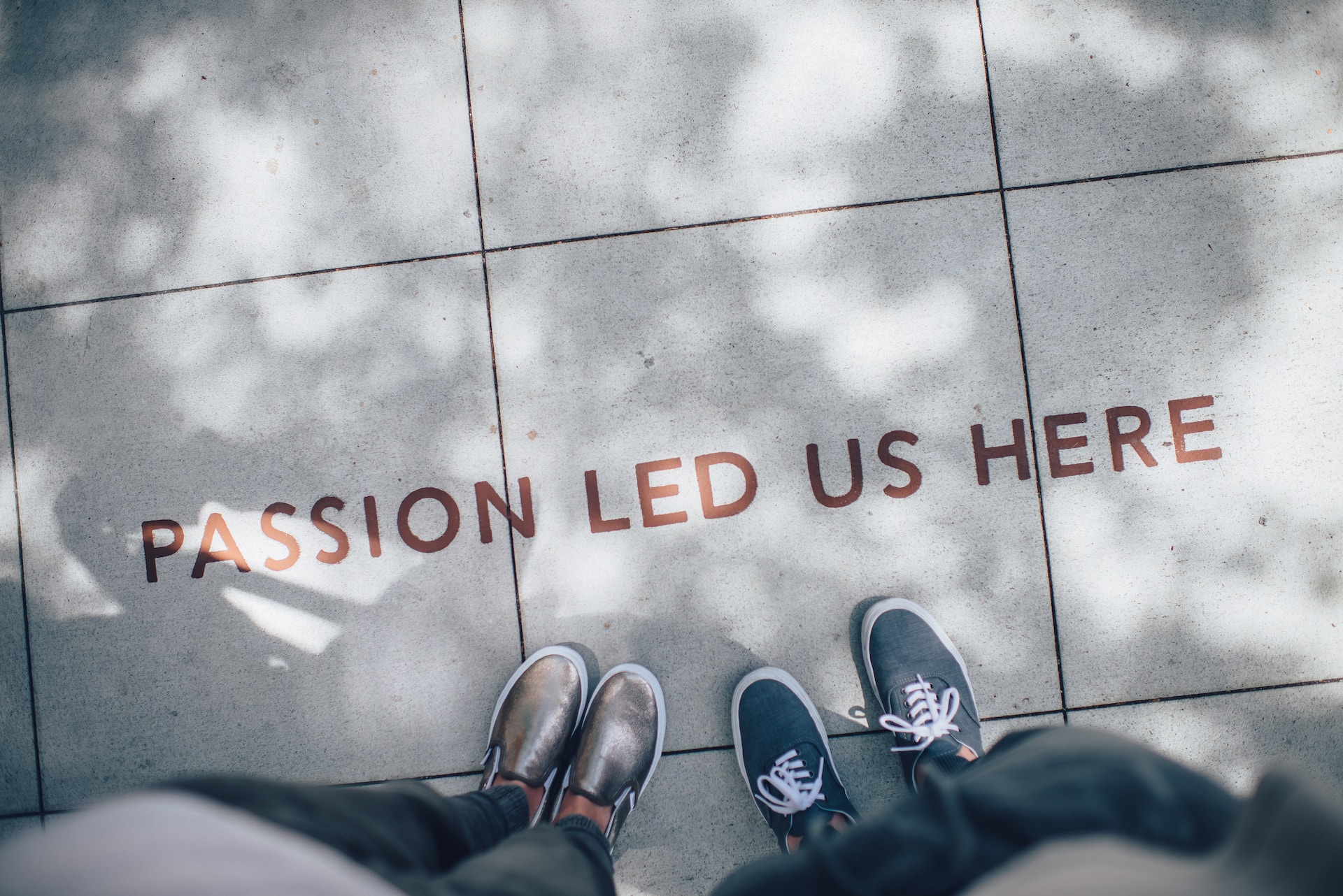 Two pairs of feet standing on pavement with the words passion led us here in front of them