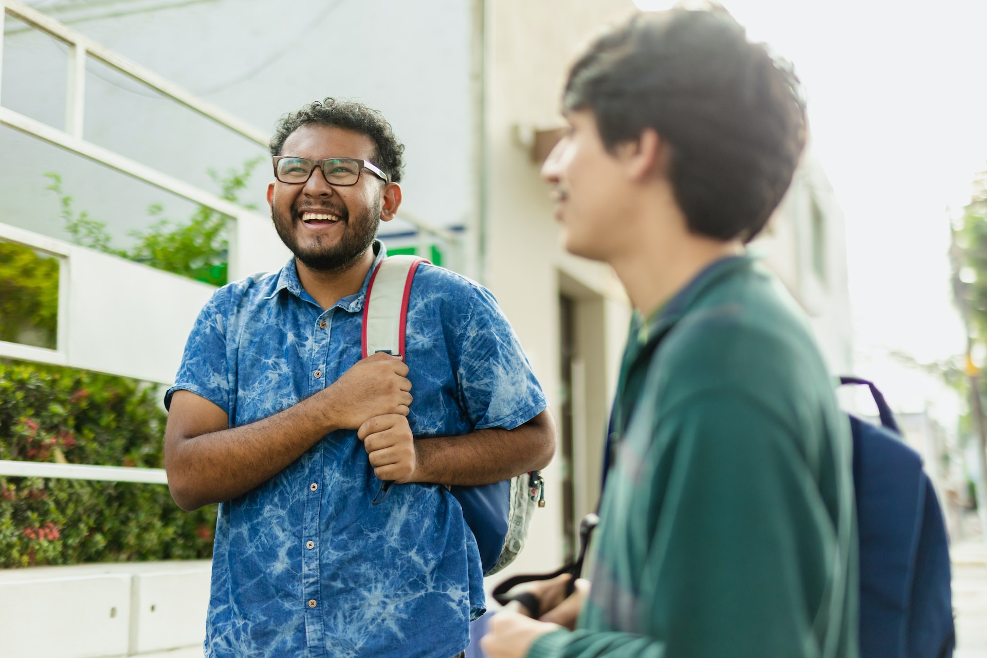 two college students with book bags standing on campus smiling while talking