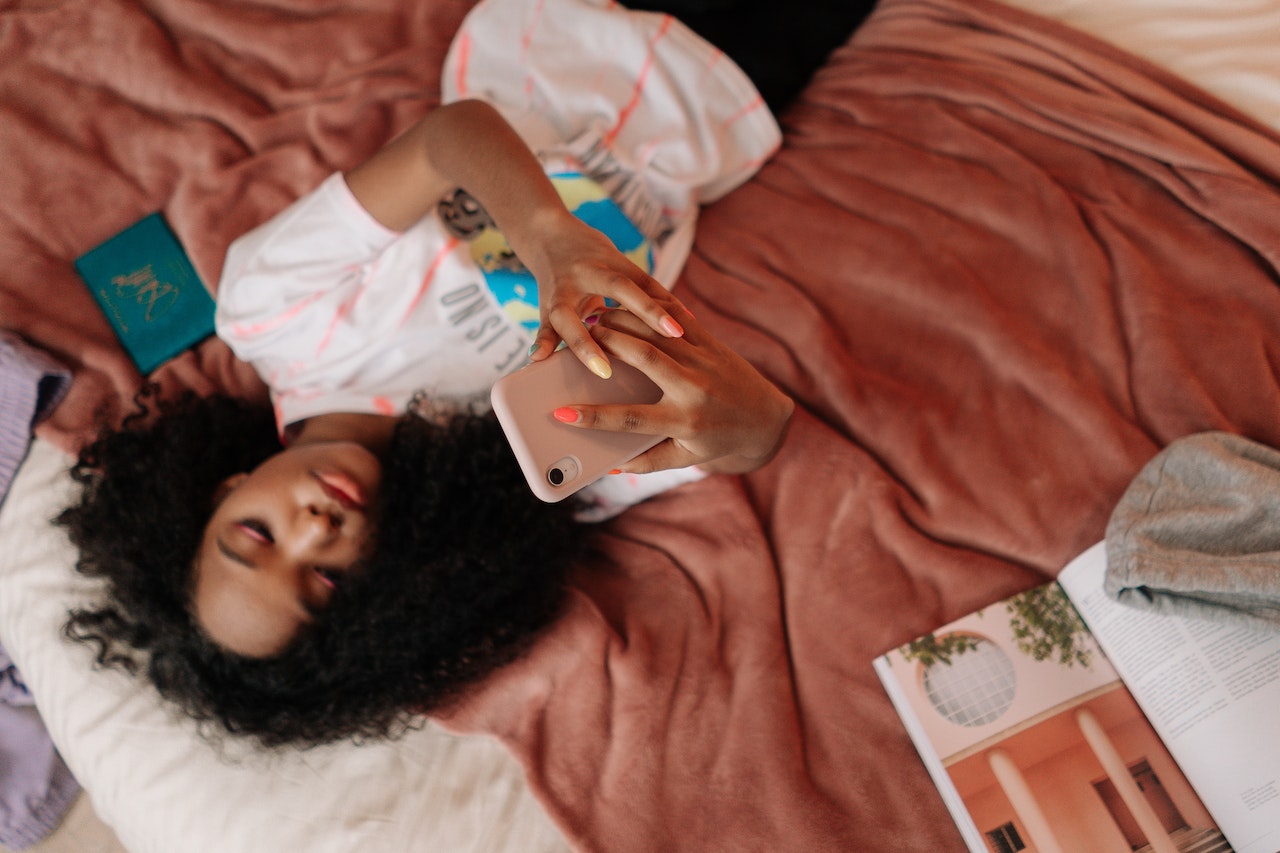 young person laying on bed looking up at her mobile phone in her hand