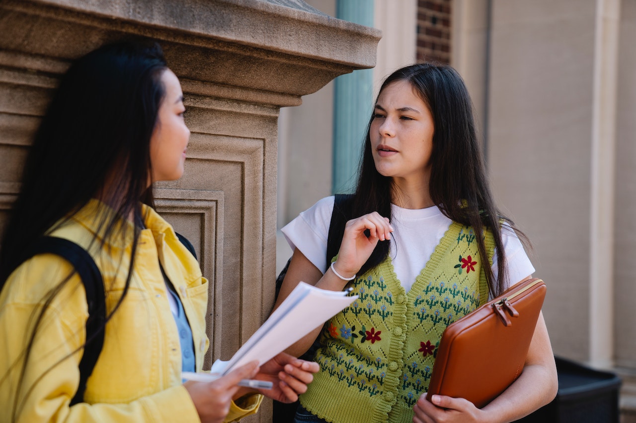 two college students talking on campus with one looking puzzled, trying to understand if she is being peer pressured into something