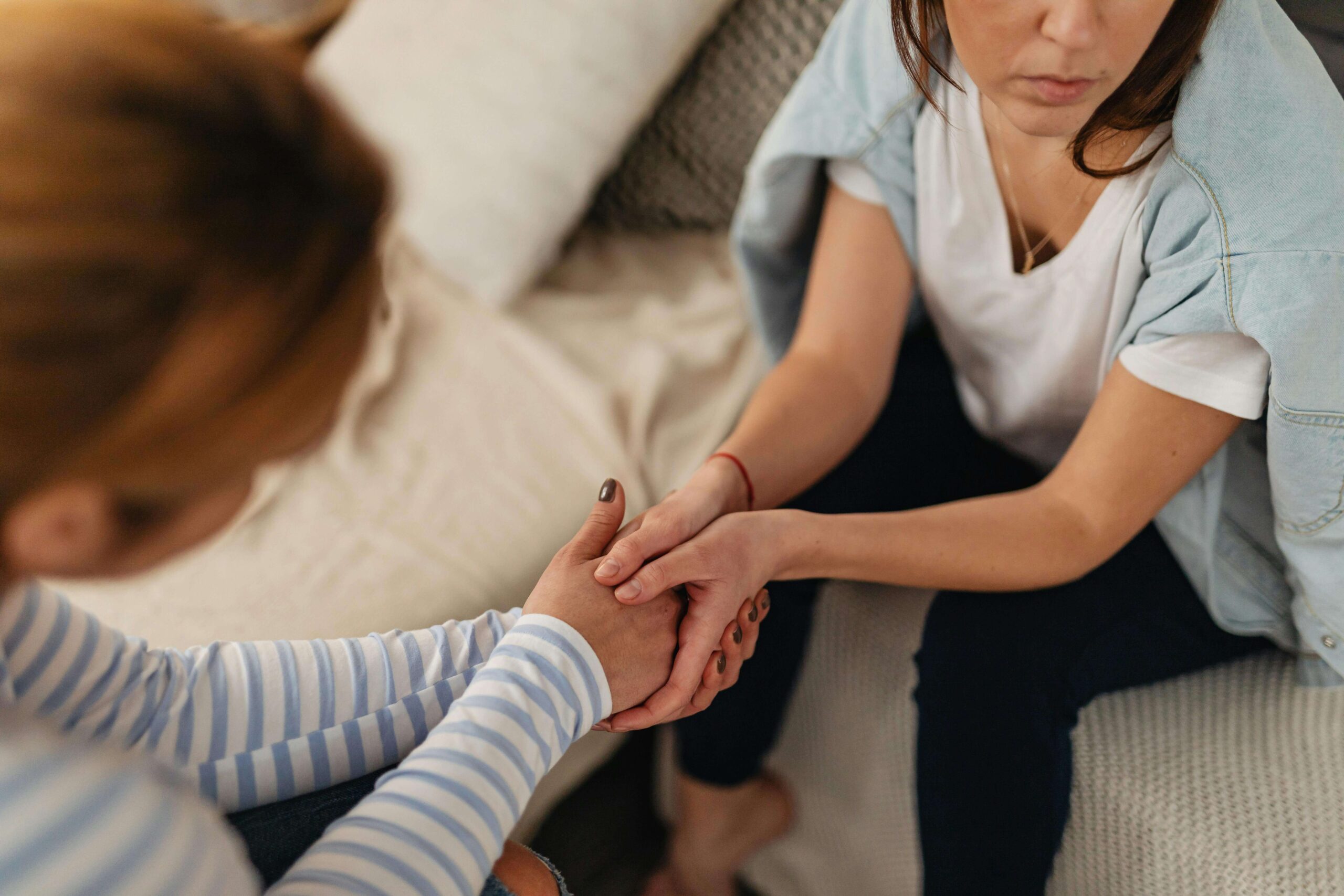 Two people sitting with their hands clasped together as part of a difficult but supportive conversation.