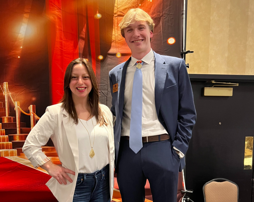 Dr. Thea Zunick, JED’s Director of Community Giving, smiles on stage at the annual District Convention (DCON), standing beside Luke McCormick.